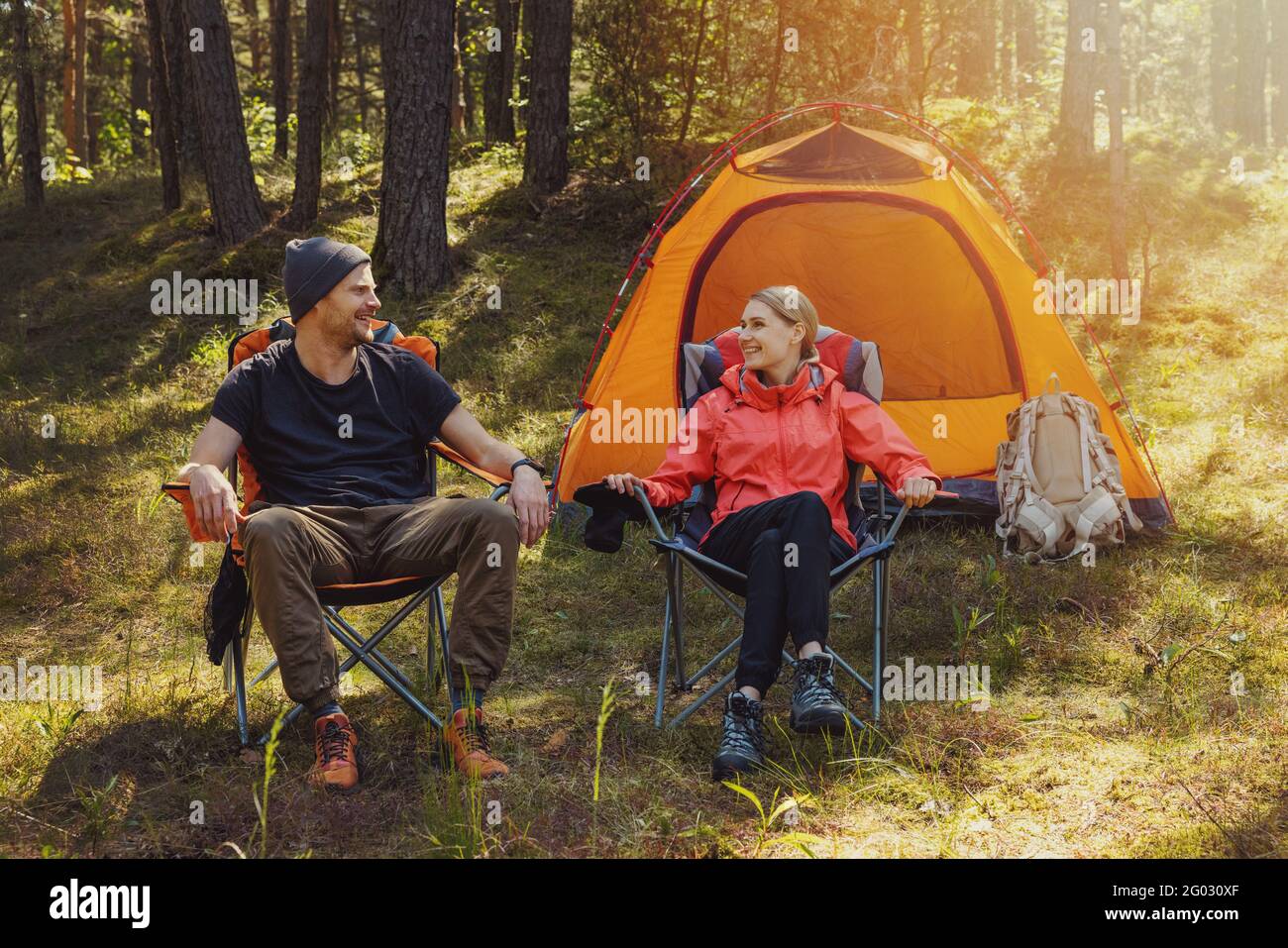 Glückliches Paar, das sich nach der Wanderung in Campingstühlen auf dem Campingplatz entspannt Im Wald Stockfoto