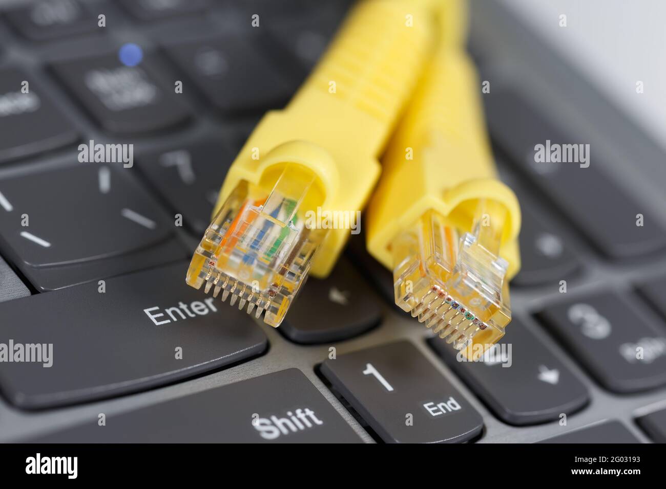 An der Laptop-Tastatur befinden sich zwei RJ-45-Anschlüsse mit einem gelben Kabel. Stockfoto