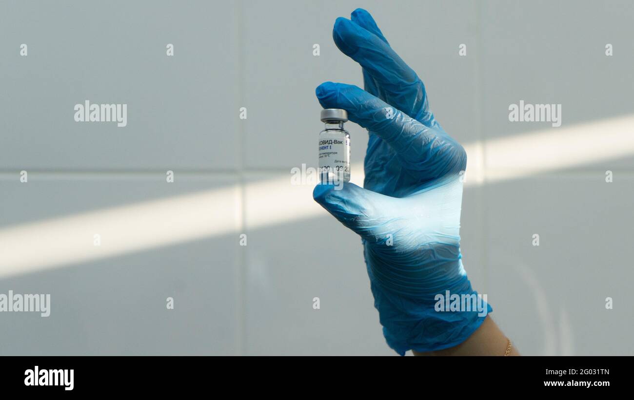 Moskau, Russland - 9. Dezember 2020, Hand in Handschuhe halten Ampulle der russischen Sputnik V-Impfstoff. Nahaufnahme. Sonnenstrahl an der weißen Wand Stockfoto