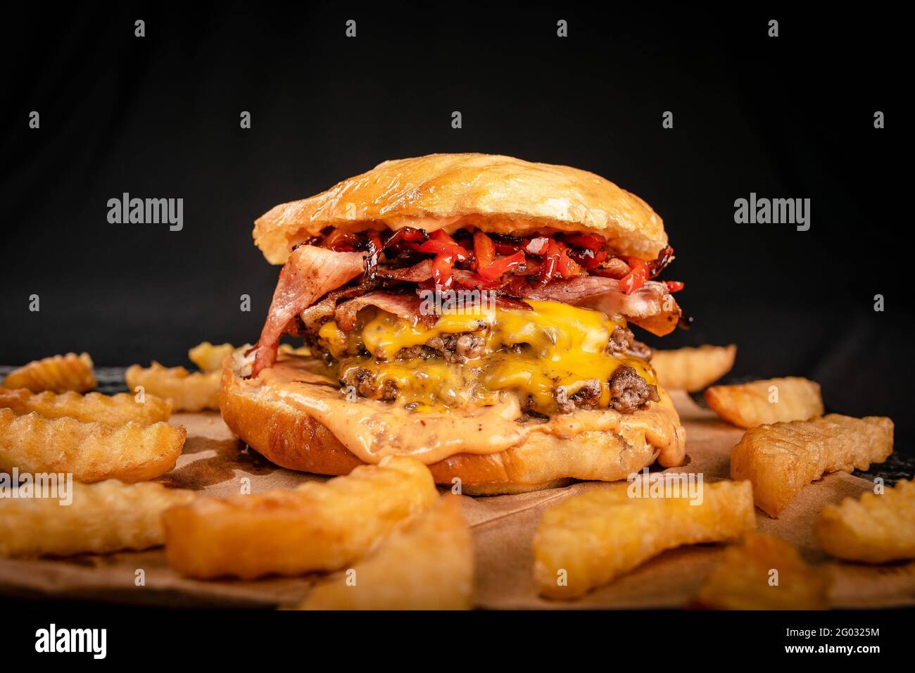 Großer handgemachter Burger mit viel Speck, Käse und Pommes auf schwarzem Hintergrund Stockfoto