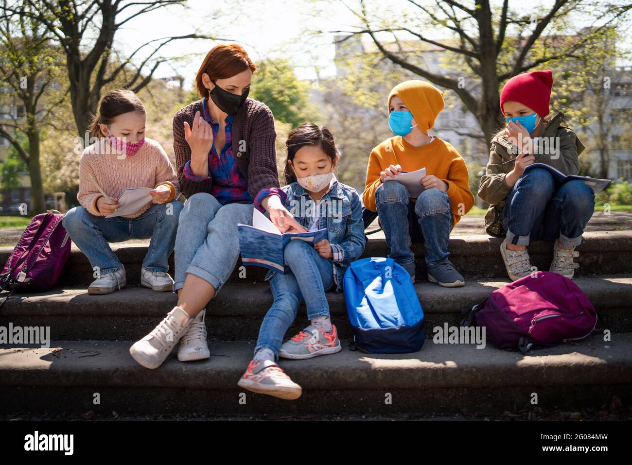 Lehrer mit kleinen Kindern, die im Stadtpark sitzen, lernen Gruppenbildung und Coronavirus-Konzept. Stockfoto