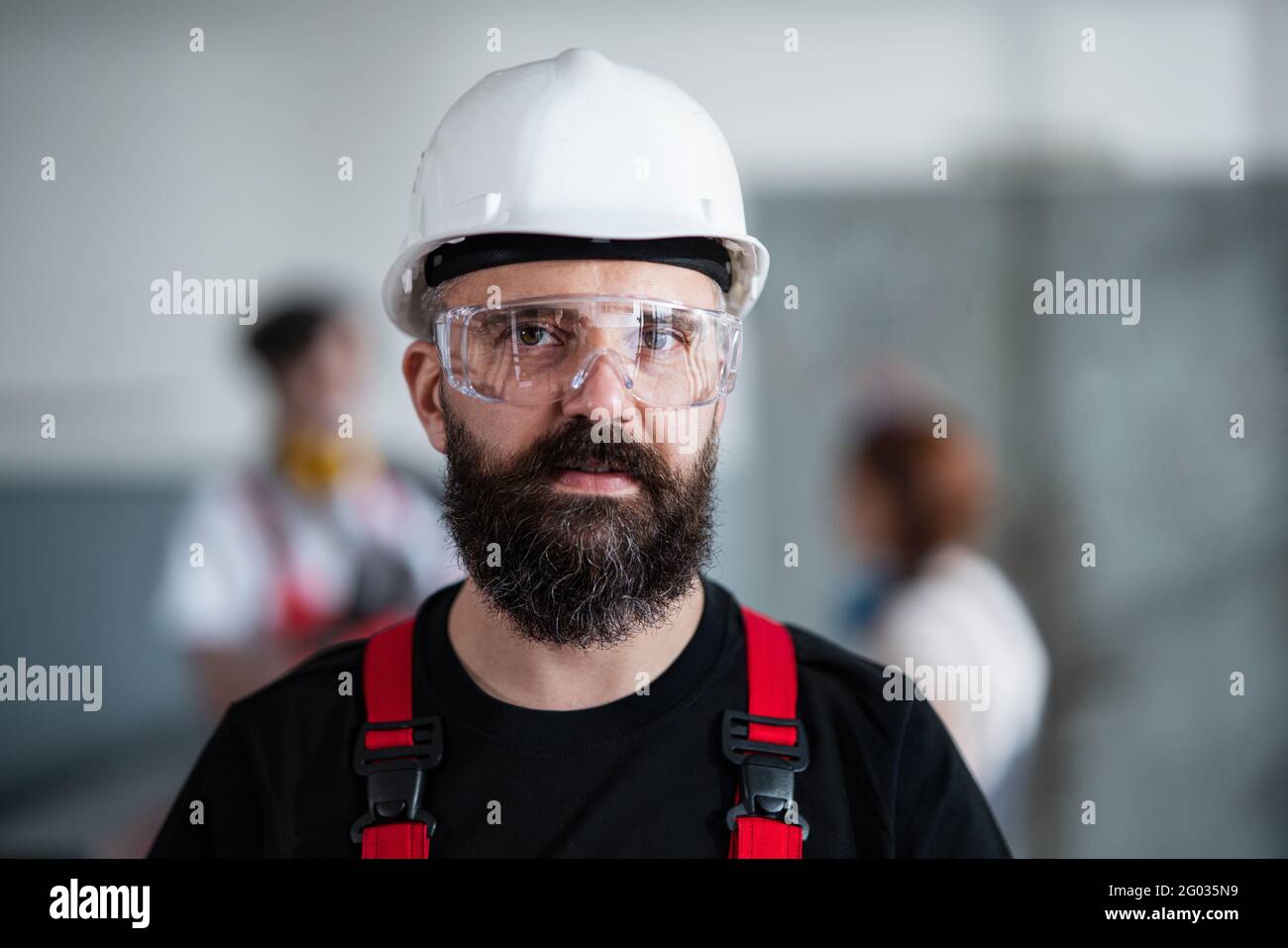 Porträt eines Arbeiters mit Helm und Schutzbrille in der Fabrik, der die Kamera anschaut. Stockfoto