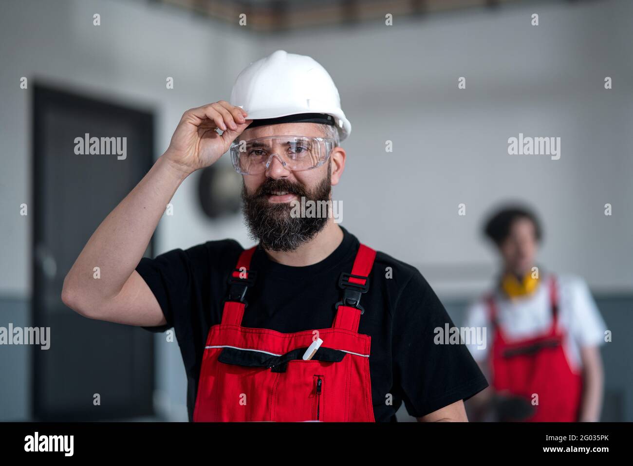 Porträt eines Arbeiters mit Helm und Schutzbrille in der Fabrik, der die Kamera anschaut. Stockfoto