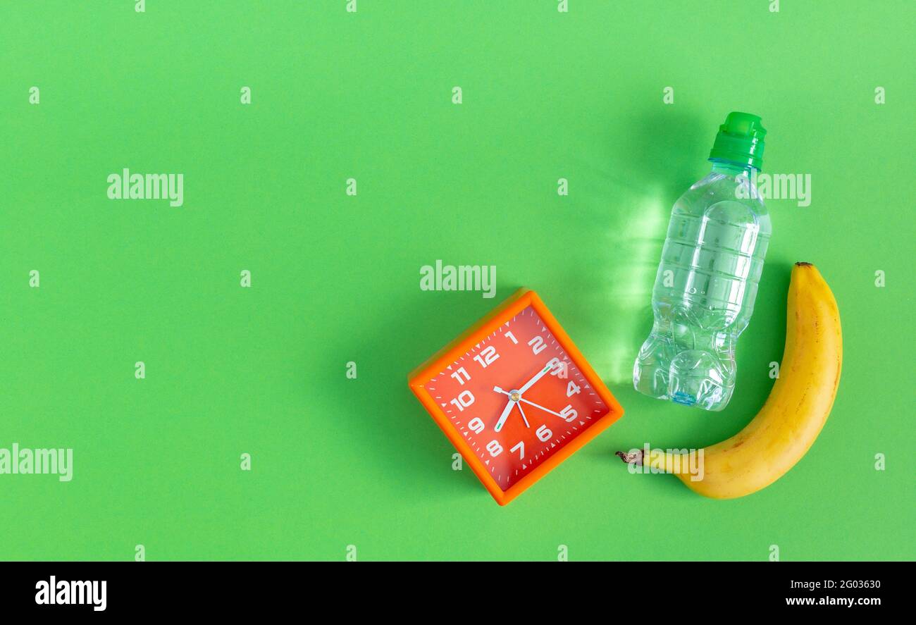 Eine Flasche stilles Wasser, Banane und ein Wecker auf grünem Hintergrund. Stockfoto