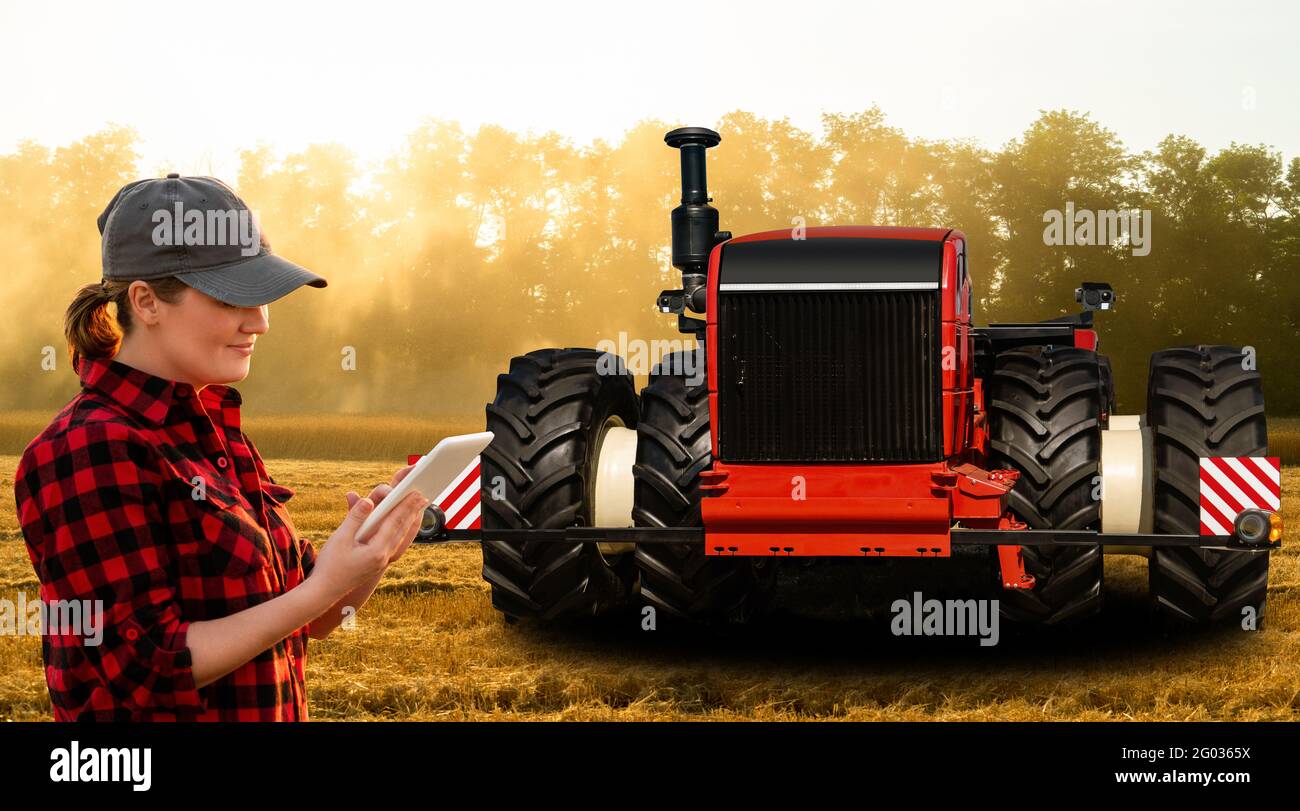 Eine Farmerin mit digitalem Tablet steuert einen autonomen Traktor an Eine intelligente Farm Stockfoto