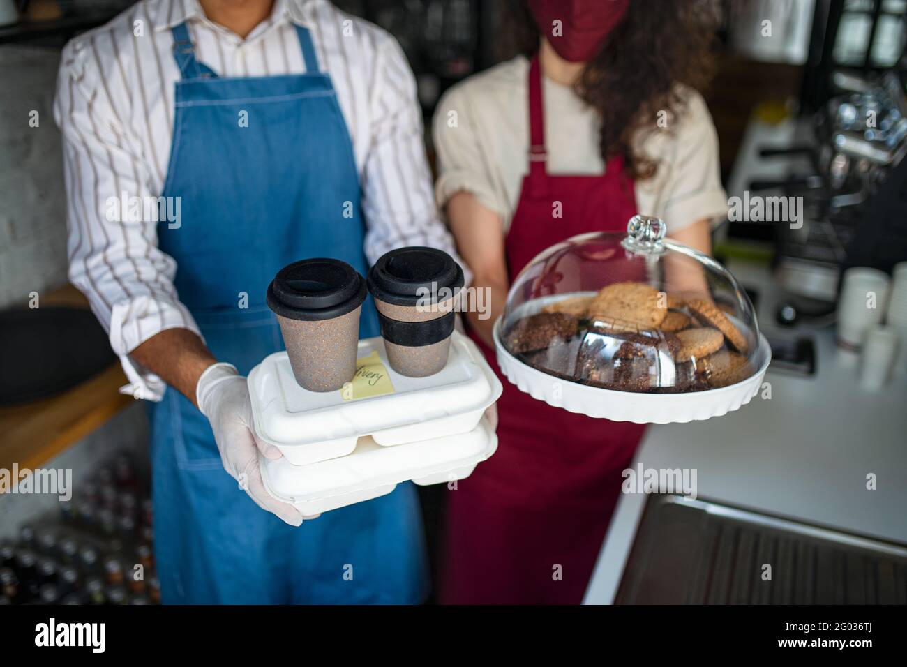 Nicht erkennbare Kellner, die einen Take-Away-Auftrag vorbereiten und die Kamera betrachten. Coronavirus-Konzept. Stockfoto