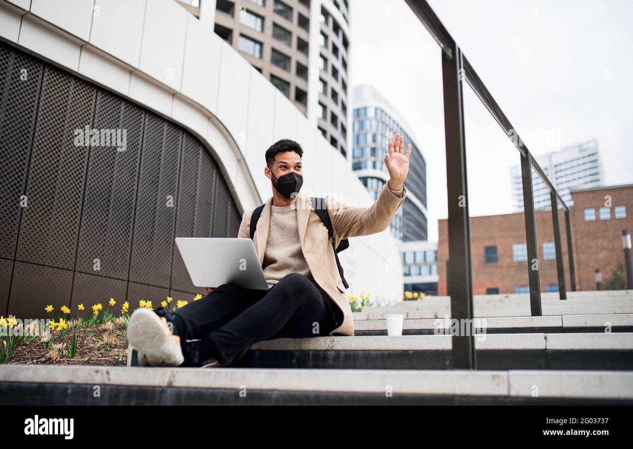 Glücklicher Mann mit Laptop, der auf dem Weg zur Arbeit im Freien in der Stadt ein Notebook verwendet, das Coronavirus-Konzept. Stockfoto