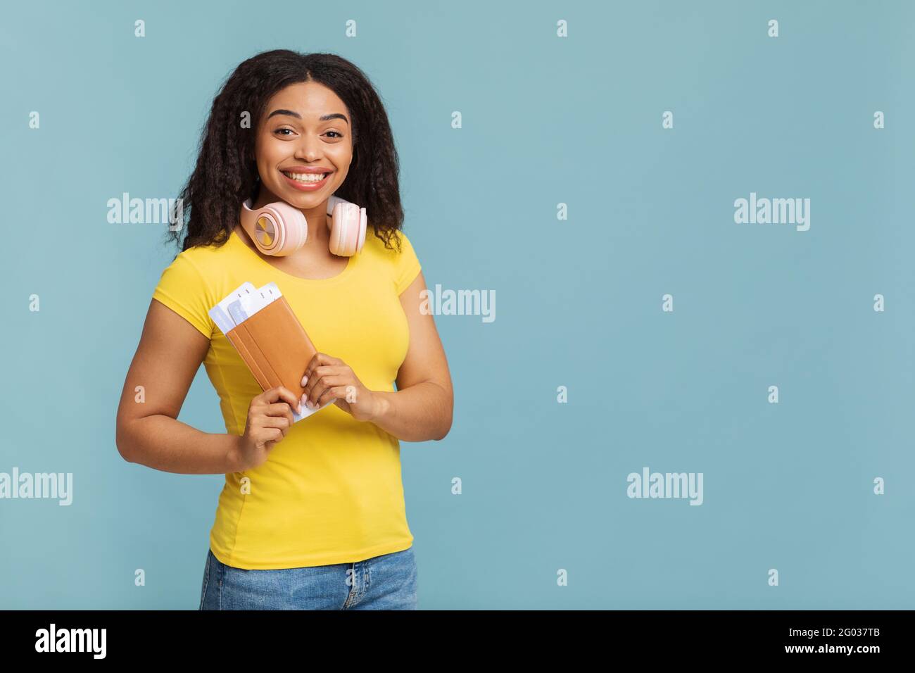 Reisekonzept. Fröhliche afroamerikanische Dame mit Kopfhörern, die Tickets auf blauem Studiohintergrund hält, freier Platz Stockfoto