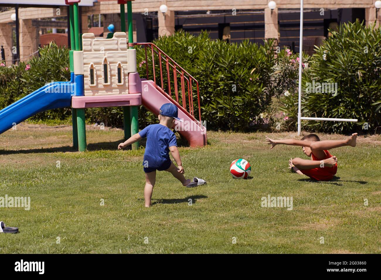 Kemer, Türkei - Mai, 21: Kleinkind und Teenager spielen bei sonnigem Wetter auf grünem, frischem Rasen Fußball. Konzept von sozialer Distanz, Sommerspaß und Urlaub. Hochwertige Fotos Stockfoto