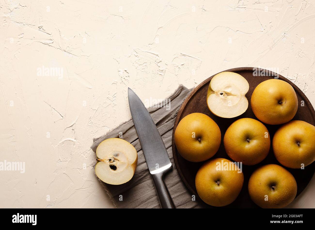Asiatische Birnen mit einem silbernen Messer auf einem Holzteller und einem braunen Stück Tuch auf einem hellen Hintergrund. Stockfoto