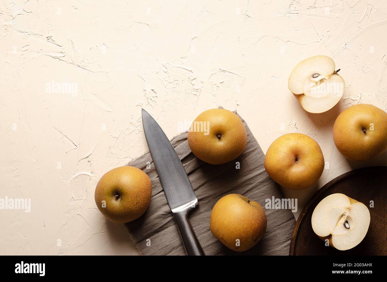 Asiatische Birnen mit einem silbernen Messer auf einem Holzteller und einem braunen Stück Tuch auf einem hellen Hintergrund. Stockfoto