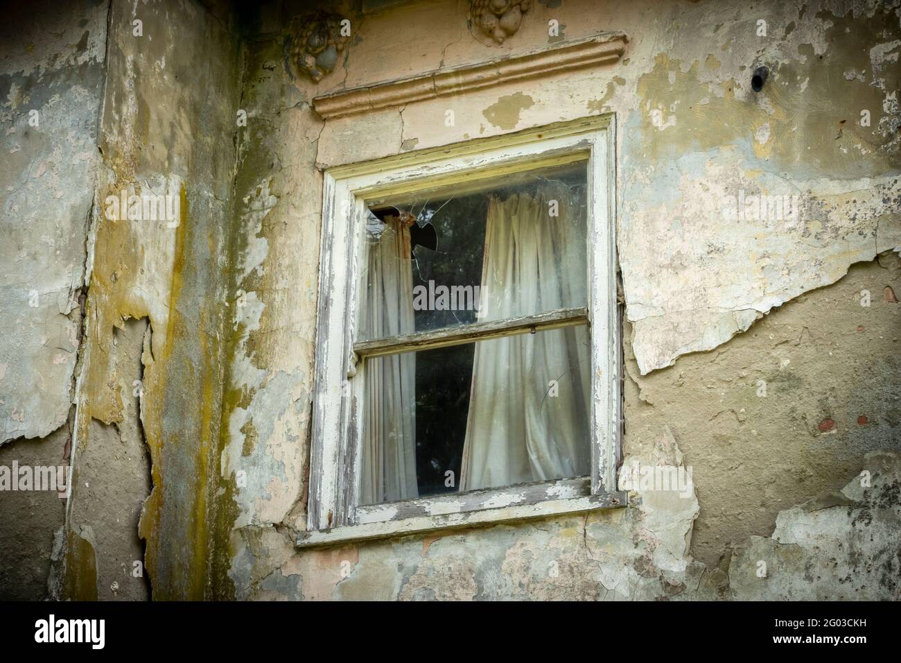 Ein beschädigtes Schiebefenster mit Vorhangsresten in einem verlassenTeil zerstörten Haus Stockfoto