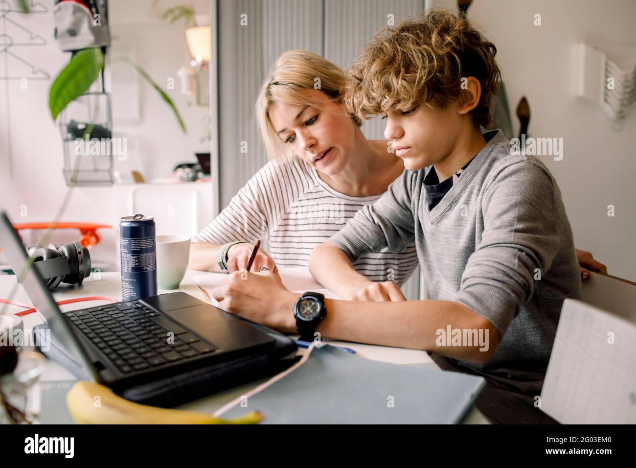 Mutter führt Sohn Hausaufgaben machen, während sie am Tisch sitzt Stockfoto