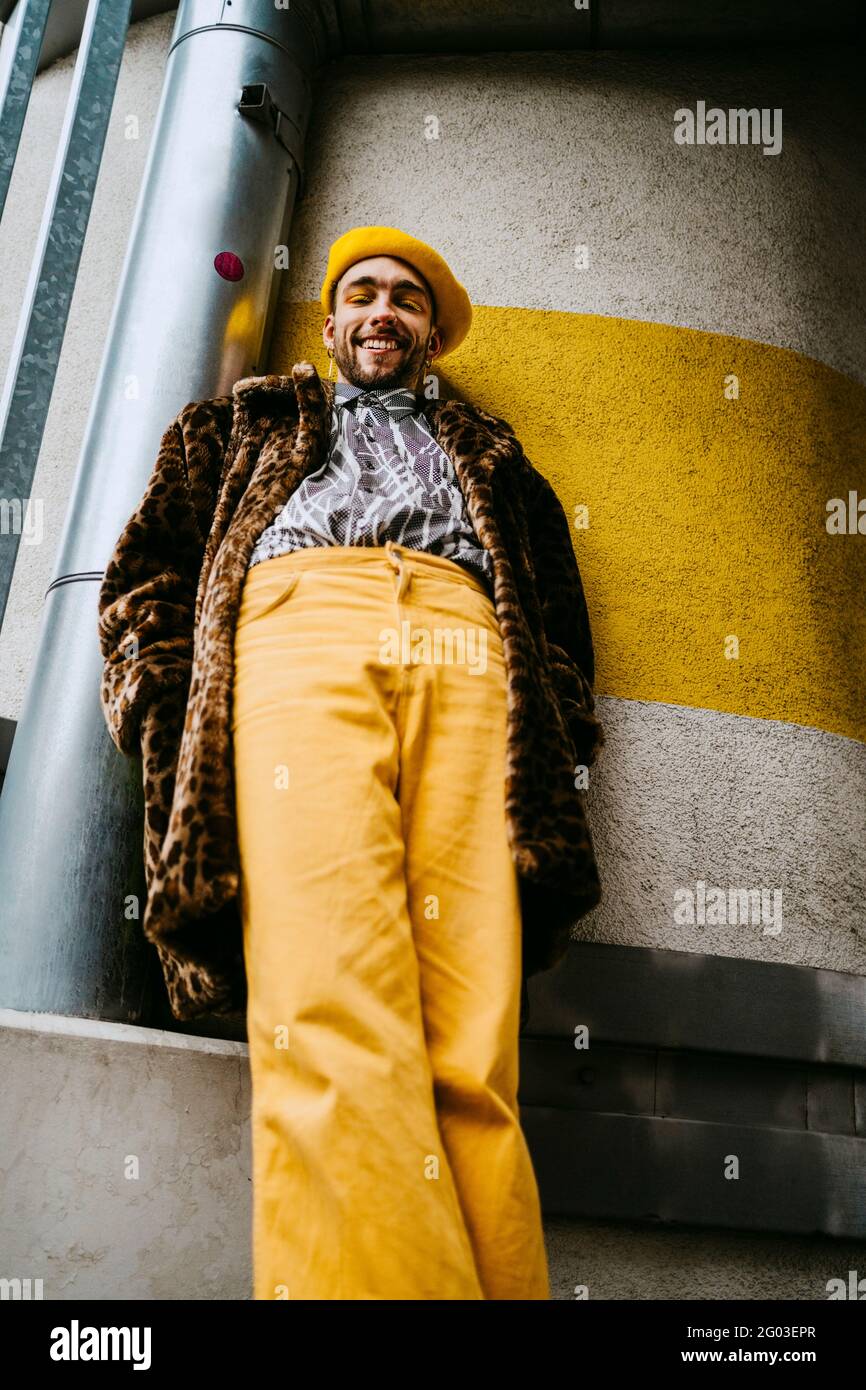 Lächelnder junger Mann mit Händen in Taschen, die gegen die Wand stehen Stockfoto