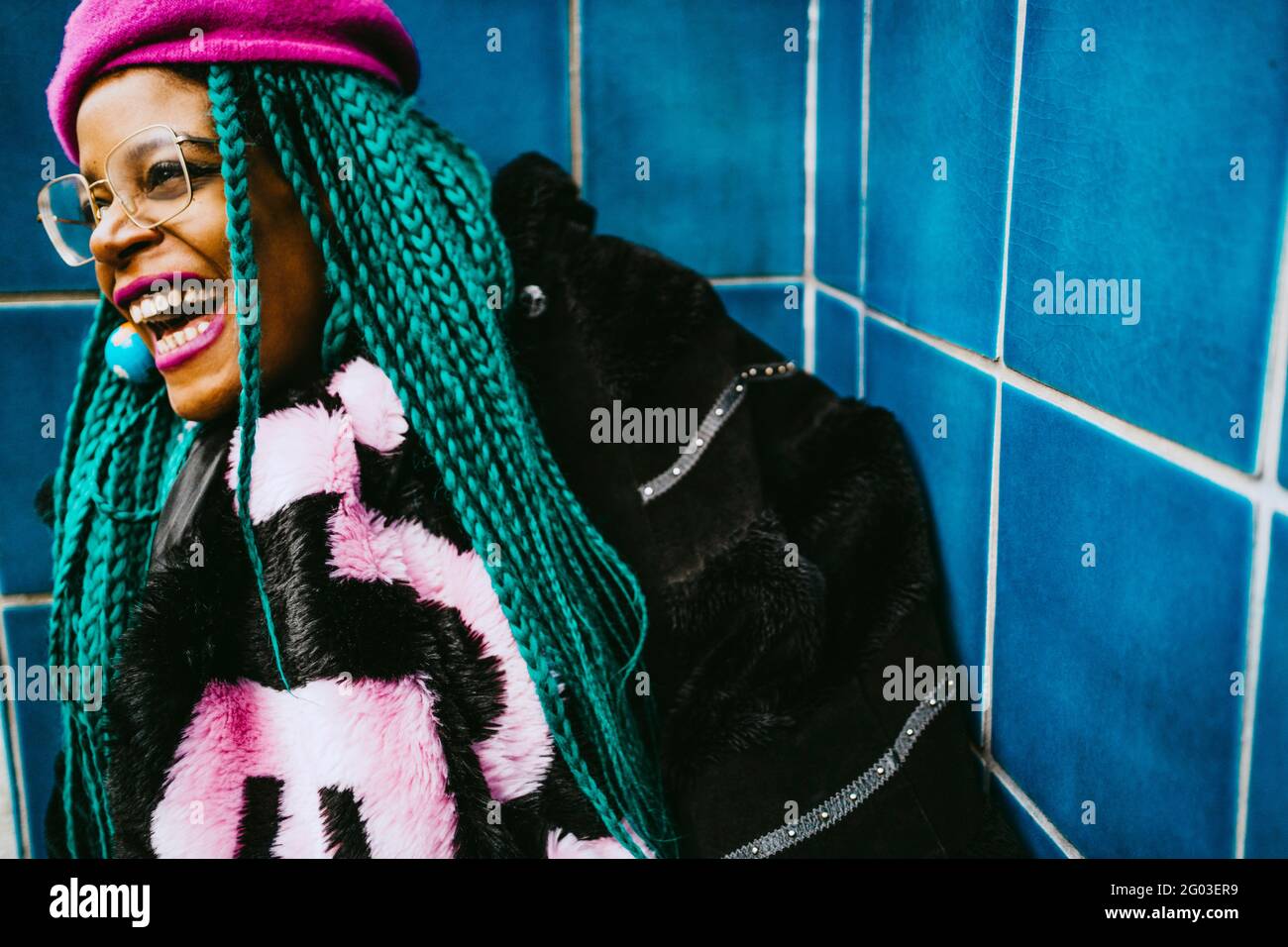 Fröhliche Frau mit mittleren Erwachsenen und geflochtenen Haaren an der blau gefliesten Wand Stockfoto