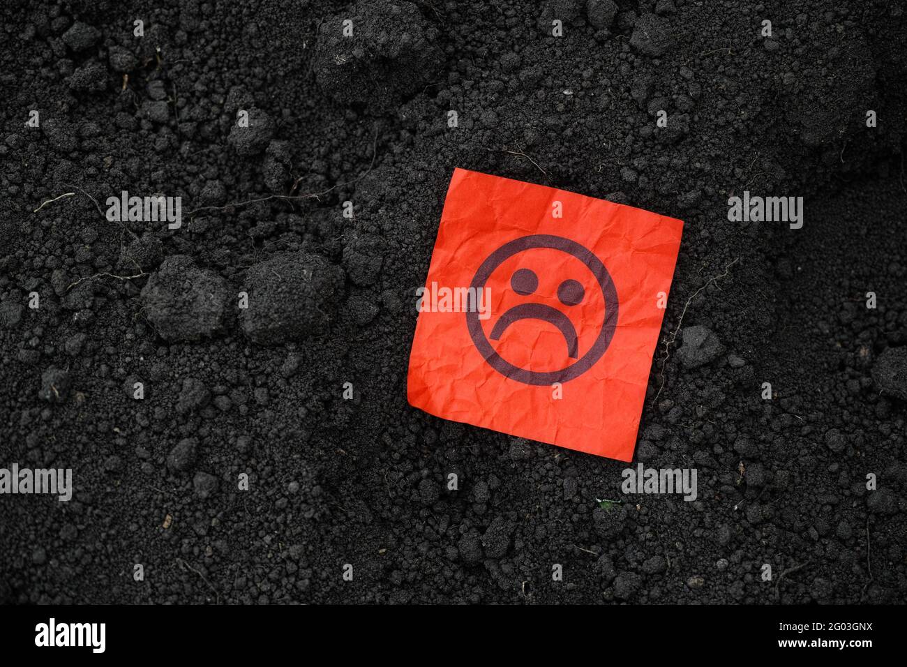 Eine rote Papiernote mit einem traurigen Gesicht auf dem Boden. Nahaufnahme. Stockfoto