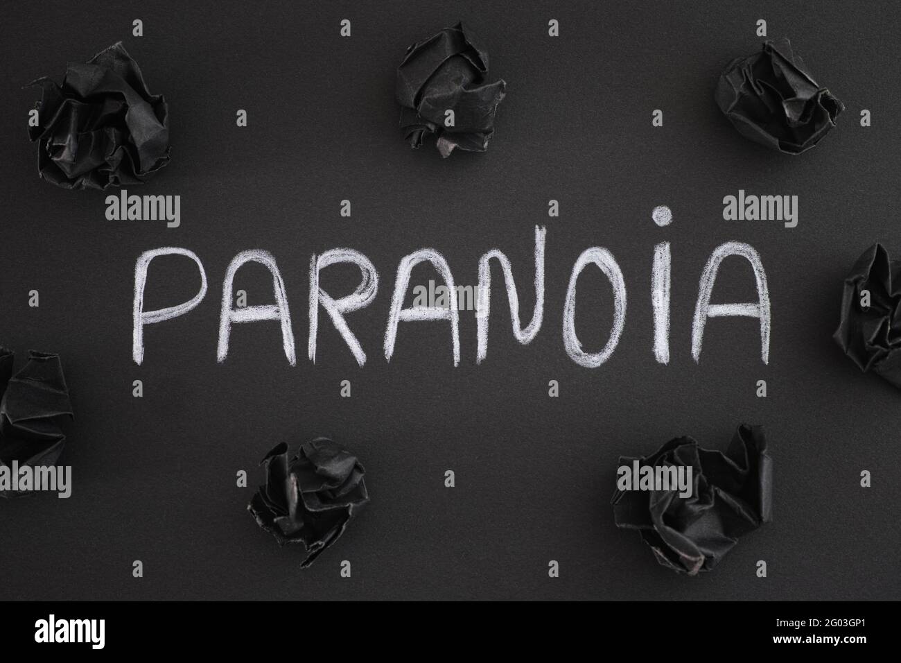 Das Wort Paranoia auf einem schwarzen Hintergrund mit schwarzen zerknitterten Papierkugeln um es herum. Nahaufnahme. Stockfoto