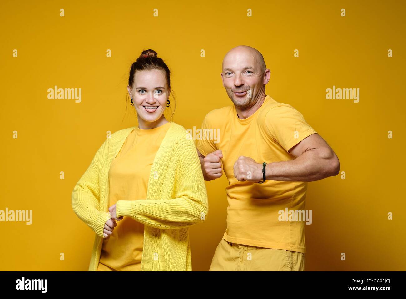 Lustige Männer und Frauen stehen in bizarren Posen und seltsamen Gesichtern. Positive Emotionen. Gelber Hintergrund. Stockfoto