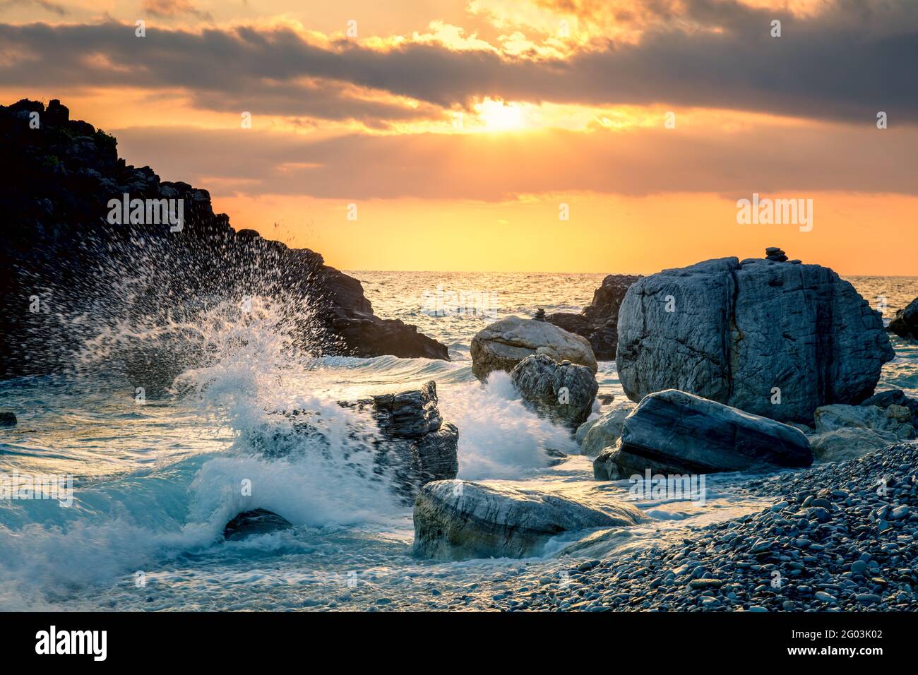 Die stürmische Ocean Wave traf am Strand auf den Felsen, das Meerwasser spritzt mit der Sonne in den Himmel. Sonnenuntergang am Meer. Sturm. Seascape. Fokus auf Vordergrund Stockfoto
