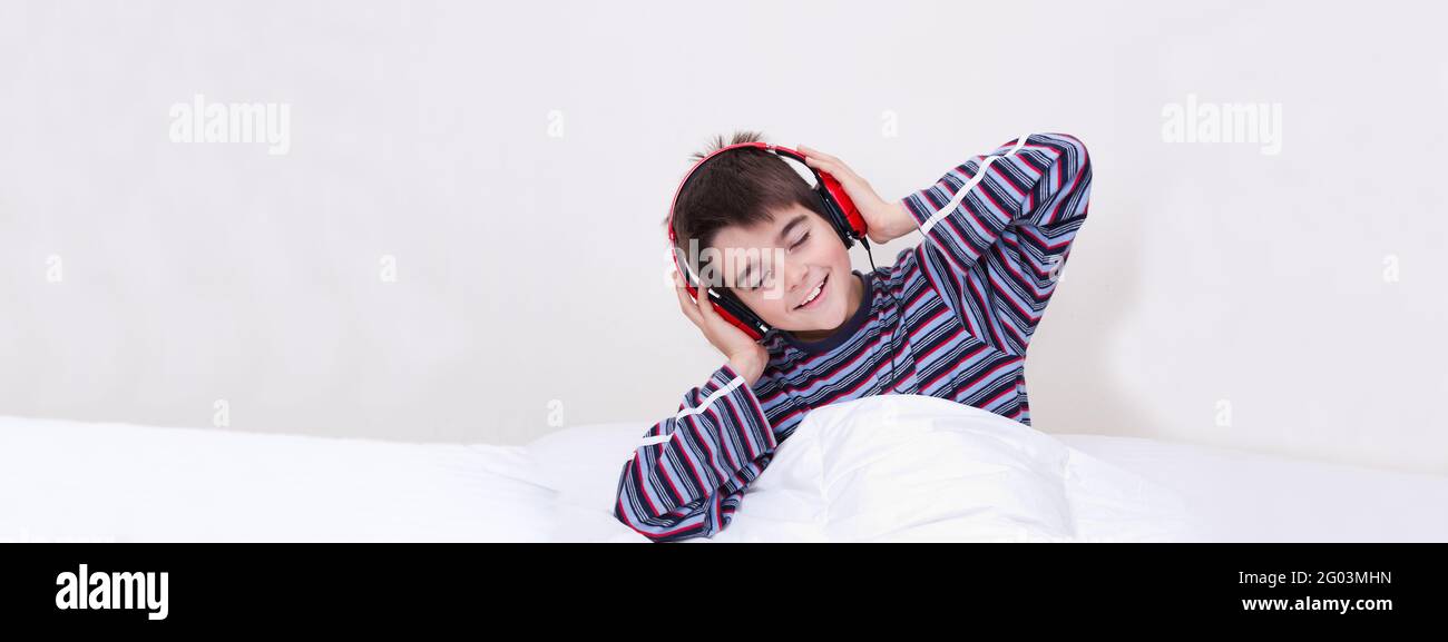 Junge im Bett, der lächelt und Musik hört, während die Kopfhörer eingeschaltet sind Weißer Hintergrund Stockfoto