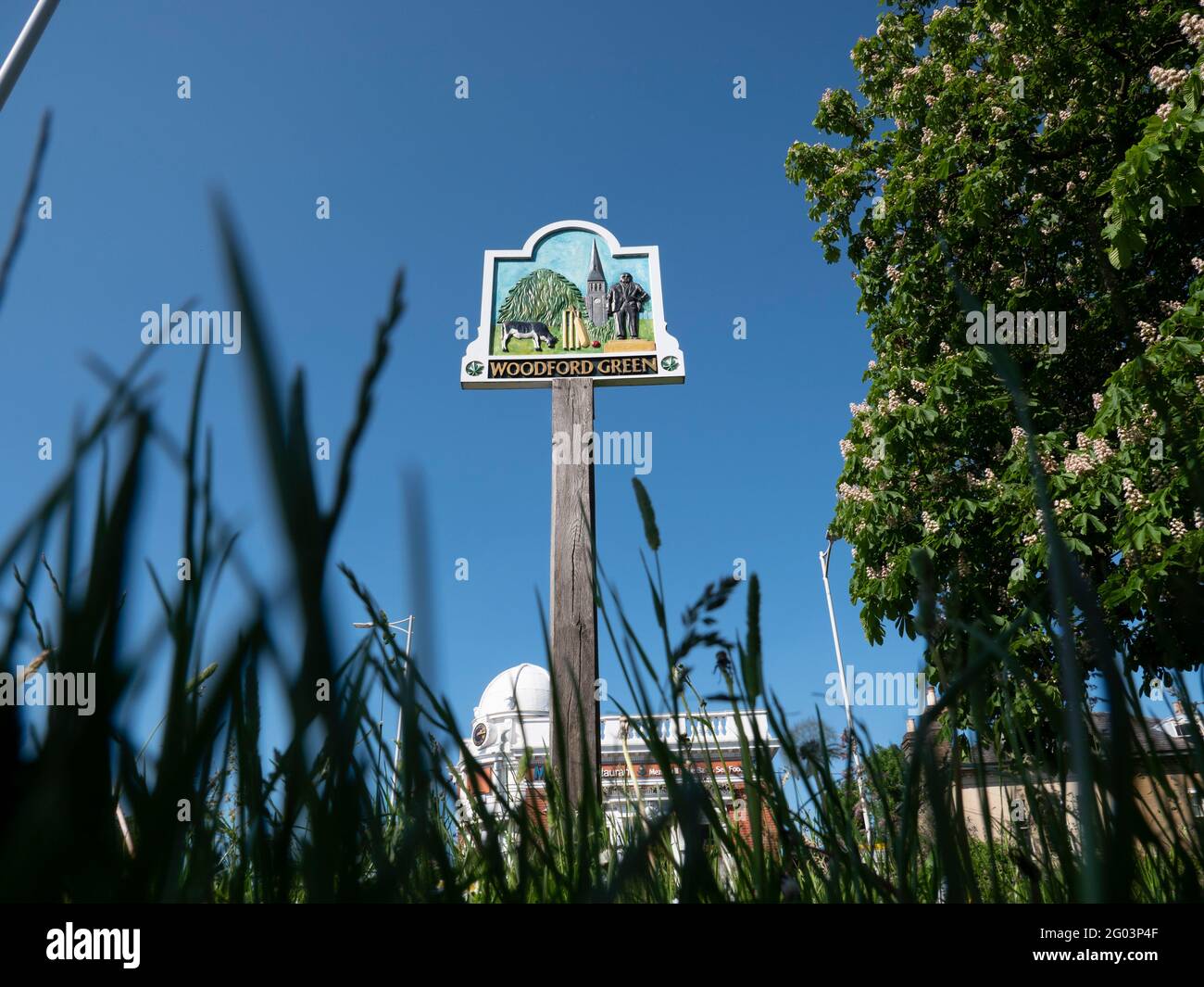 Gesamtansicht von Woodford Green im Nordosten Londons an der Grenze zu Essex, mit Woodford Green Schild auf Holzmast und Stadt im Hintergrund Stockfoto