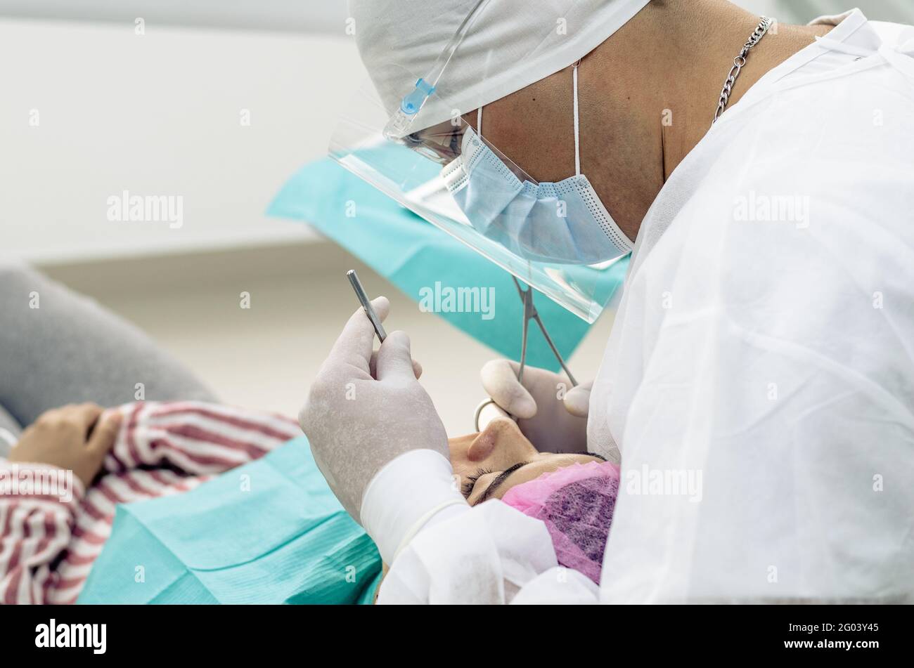 Der Zahnarzt oder Arzt trägt im Hintergrund der Zahnarztpraxis einen weißen medizinischen Kittel, eine Maske und eine Schutzbrille Stockfoto