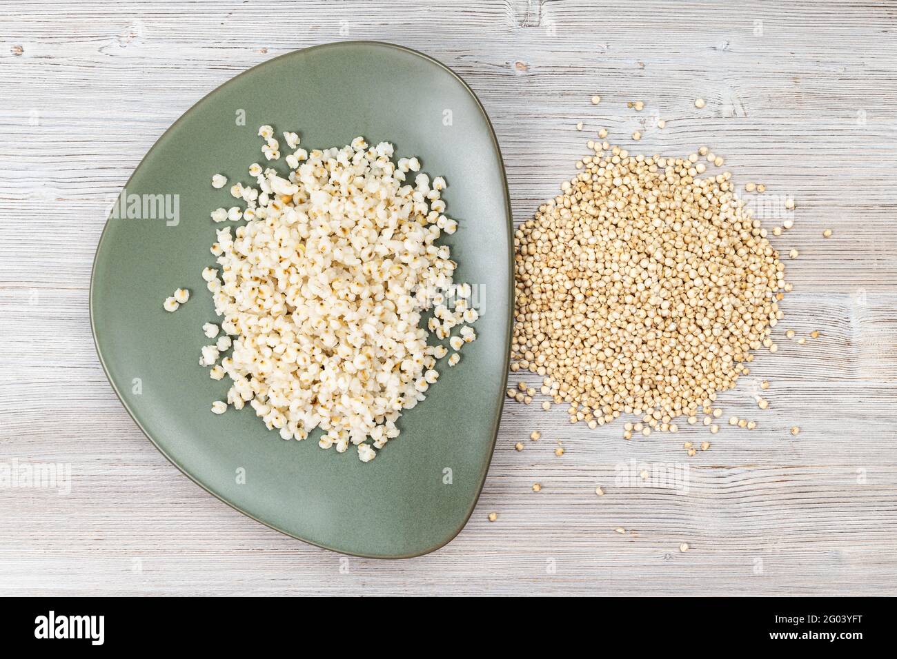 Draufsicht auf rohe Sorghum-Körner und gekochten Brei Grüner Teller auf Holztisch Stockfoto