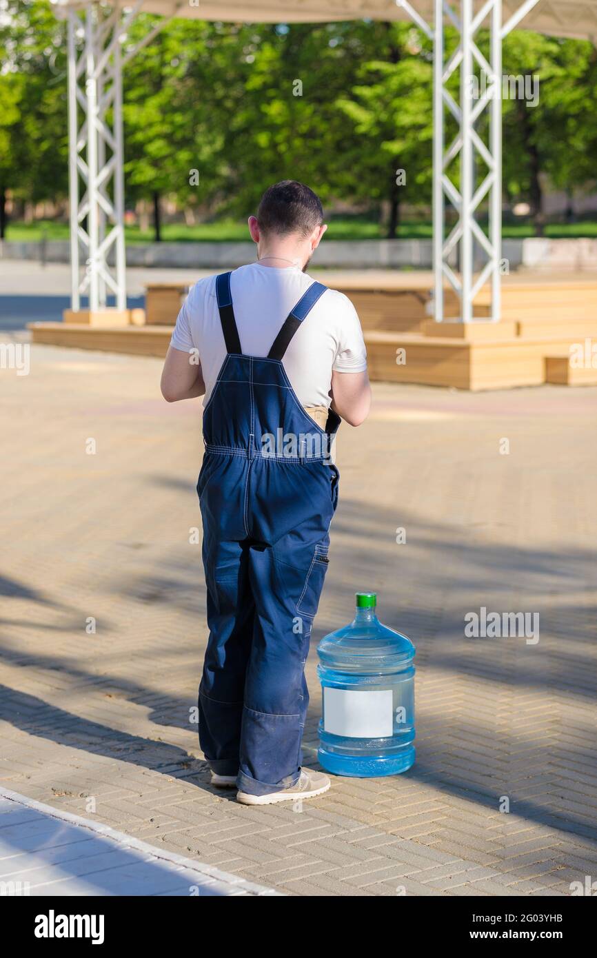 Ein erwachsener Mann in Overalls liefert Trinkwasser zu den Geschäften. Ein Arbeiter steht mit einem Barrel Trinkwasser. Stockfoto