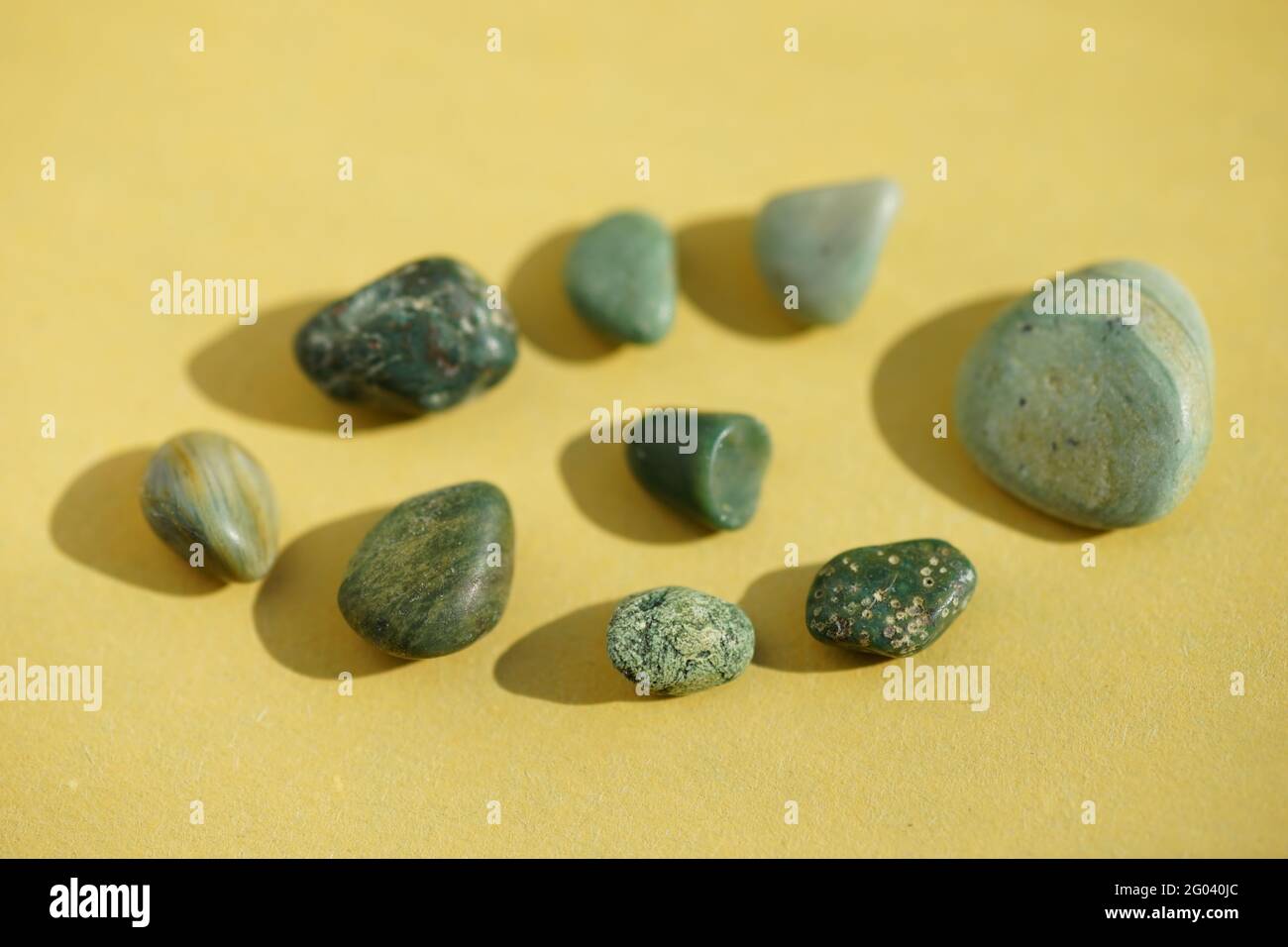 Set aus grünen Kieselsteinen an einem gelben sonnigen Tisch. Stockfoto