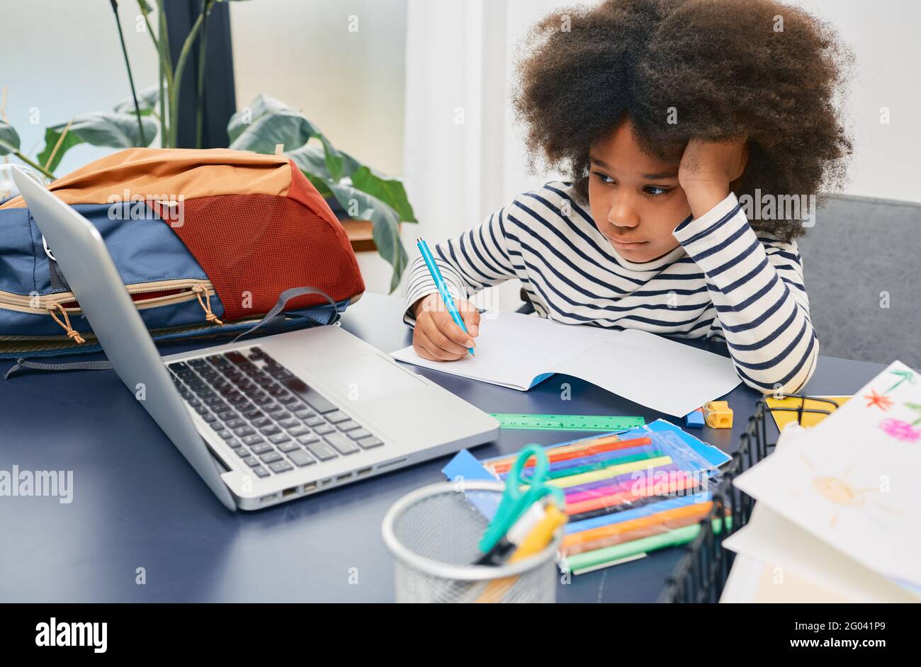 Die kleine Schülerin studiert zu Hause und macht ihre Schulaufgaben, sitzt mit einem Laptop am Tisch Stockfoto
