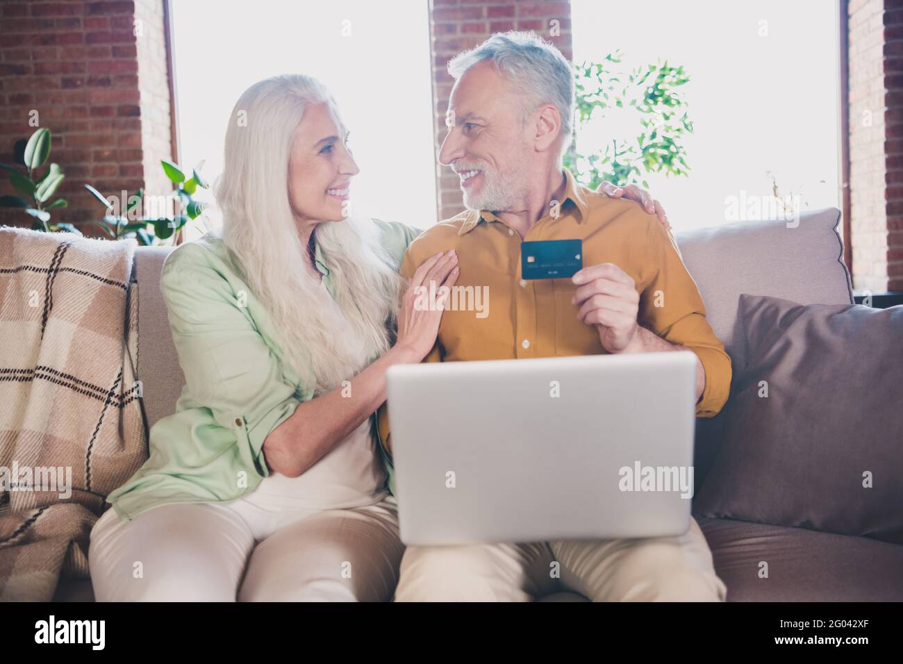 Portrait eines schönen älteren Rentners fröhliches Paar auf dem sitzt Sofa mit Karte kaufen Web-Shop zu Hause Ziegel Loft Innenhaus innen Stockfoto