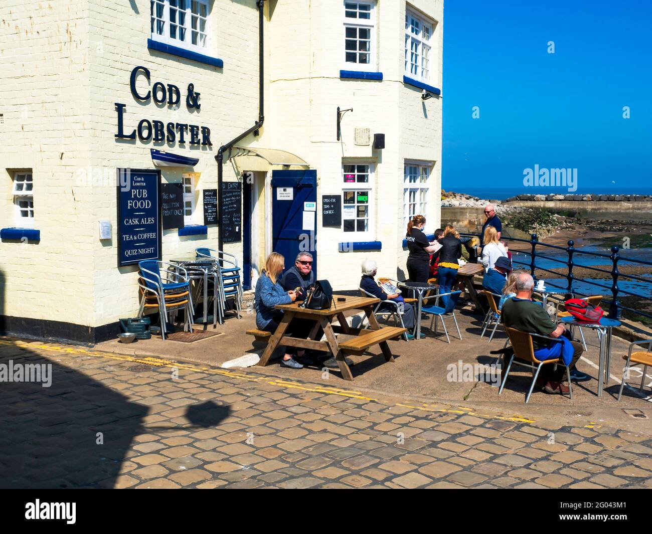 Menschen, die außerhalb des auf die Bestellung ihres Mittagessens warten Cod and Lobster Pub am Hafen von Staithes North Yorkshire im Herbst Stockfoto