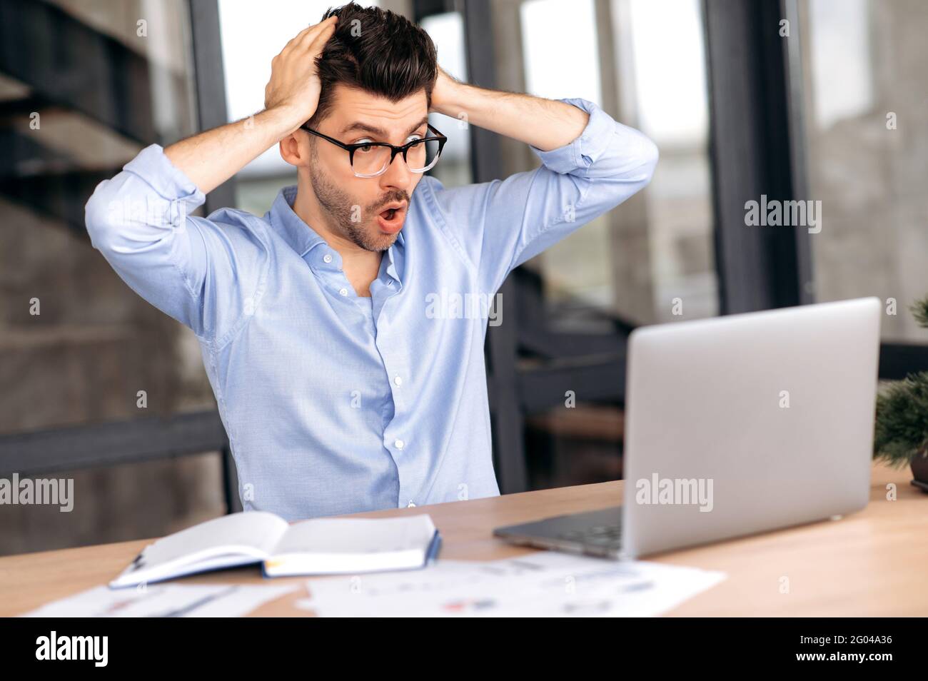 Schockiert kaukasischen männlichen Manager, Makler oder Freiberufler, arbeiten im Büro, mit Laptop, mit großen Verlusten, Überarbeitet, gestresst, überrascht auf den Bildschirm schauend, seinen Kopf mit den Händen haltend Stockfoto