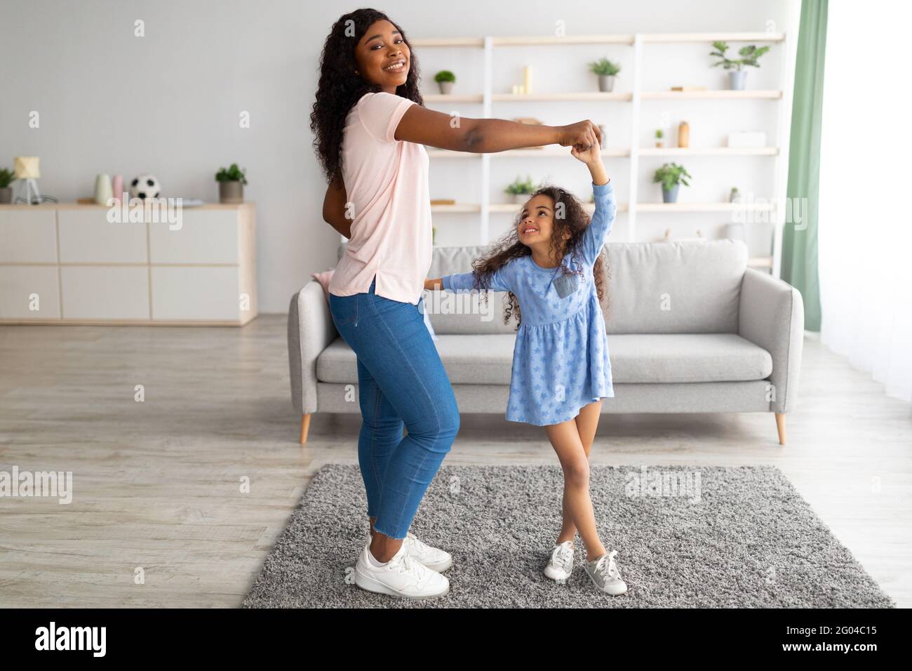 Die ganze Länge der afroamerikanischen Mutter tanzt zu Musik mit Ihre süße kleine Tochter zu Hause Stockfoto