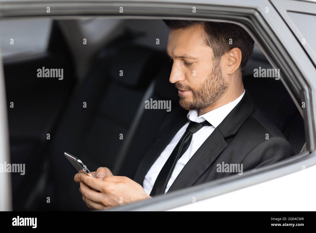 Wohlhabender Manager sitzt im Auto und benutzt Smartphone Stockfoto