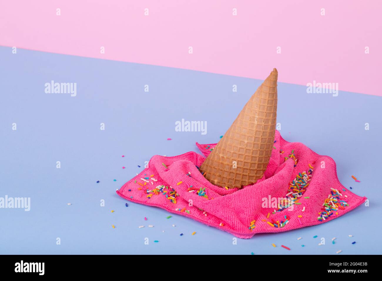 Kreative Minimalidee aus Eiscreme-Kegel und Wischtuch, das auf pastellblauem und pinkem Hintergrund verschüttet wurde. Minimalistisches Sommerkonzept von Essen und Onkel Stockfoto