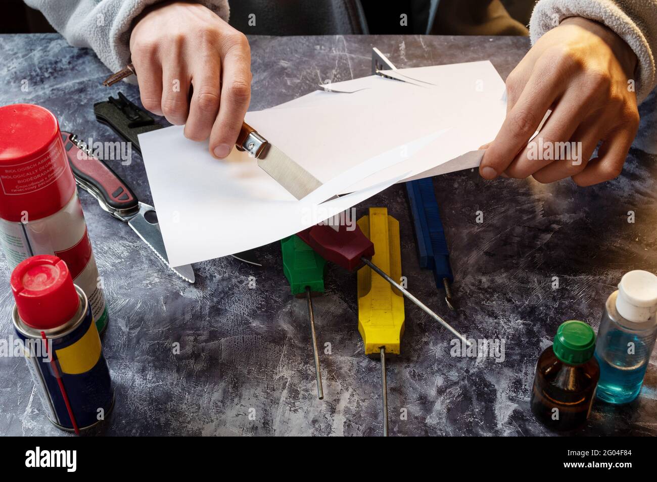 Schneiden Sie das Papier mit einem Messer. Der Meister schneidet das Papier mit einem Messer. Die Schärfe des Messers prüfen. Stockfoto