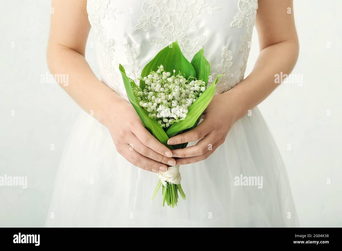 Braut mit Blumenstrauß von schönen Maiglöckchen auf hellem Hintergrund Stockfotografie