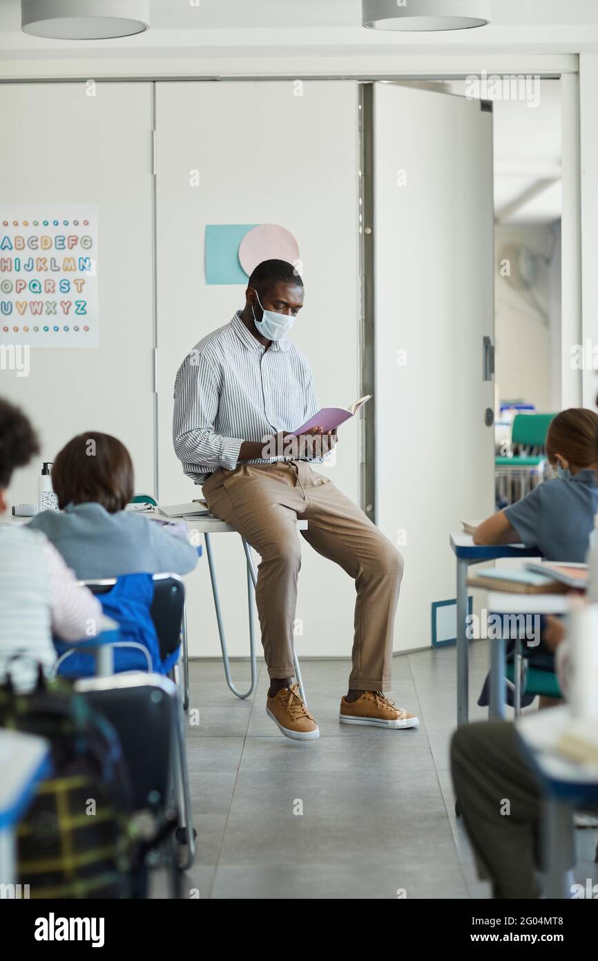 Porträt eines afroamerikanischen Lehrers in voller Länge, der im Klassenzimmer eine Maske trägt, mit Sicherheitsmassnahmen Stockfoto