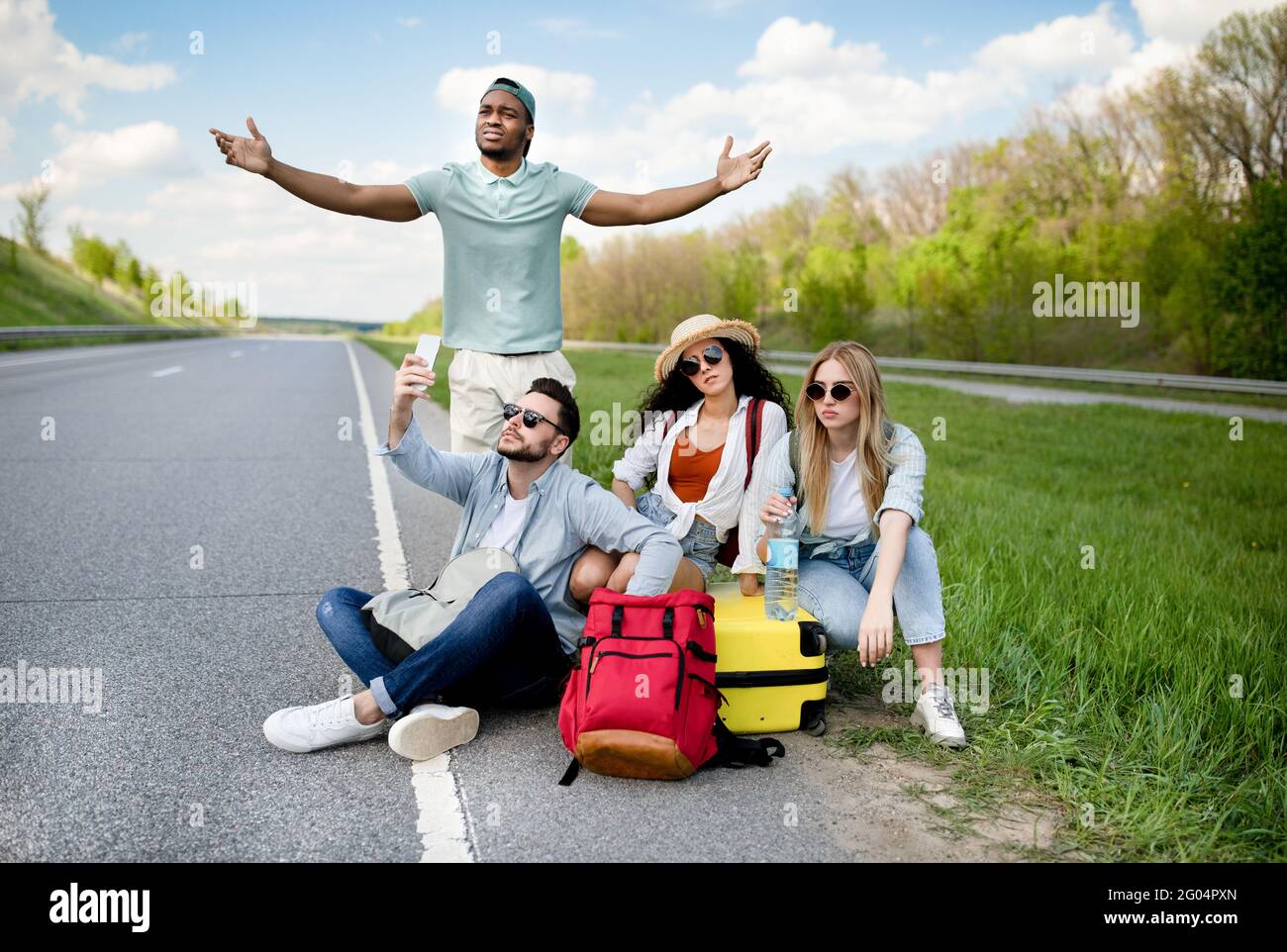 Unglückliche, tausendjährige Touristen, die am Straßenrand sitzen, können das Auto nicht fangen, warten zu lange und haben keine Smartphone-Verbindung Stockfoto