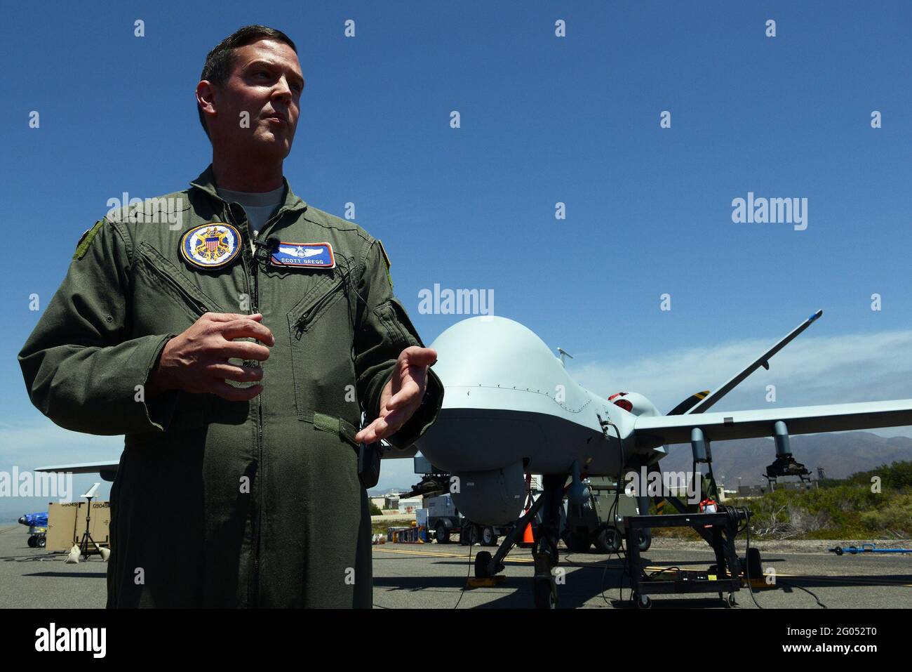 Berichterstattung: Air Force Maj. Scott Gregg, Projektleiter des Black Dart-Projekts, spricht vor einem unbemannten MQ-9 Reaper-Flugzeugsystem auf dem Marinestützpunkt Ventura County and Sea Range, Point Mugu, Kalifornien, 31. Juli 2015 mit den Medien. Die Drohne, sagte Gregg, ist in den größten Kategorien von UASs, oder Gruppe 5, fliegt auf mehr als 18,000 Fuß und wiegt mehr als 1,300 Pfund. Es wurde als Teil der zweiwöchigen Black Dart Gegen-UAS-Demonstration vom 26. Juli bis 1. August verwendet, um Technologien, Taktiken und Techniken zu bewerten und zu verbessern, die vom DoD und seinen Partnern verwendet wurden. Stockfoto