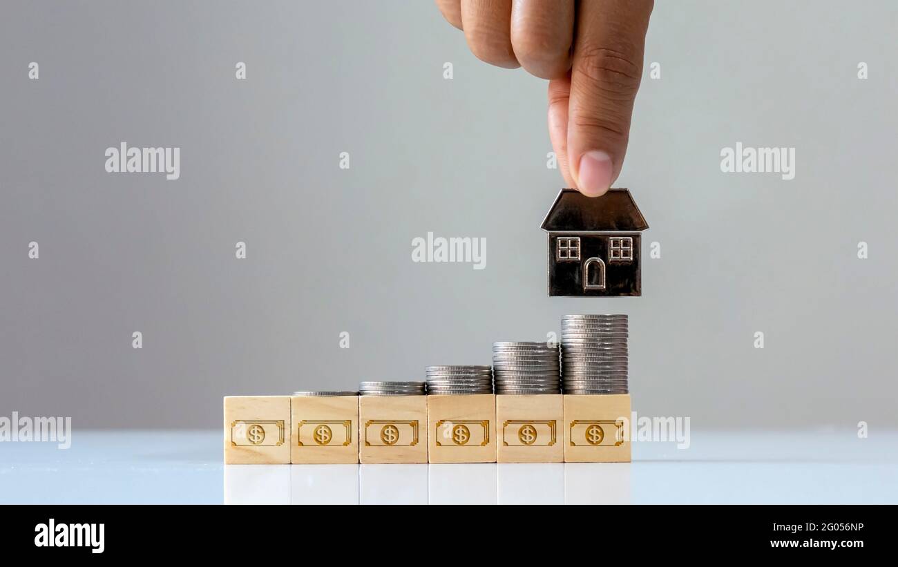 Ein Haufen Münzen auf einem Holzblock mit einem Geldsymbol und einem mobilen Finanz- und Investitionskonzept über Immobilienunternehmen. Stockfoto