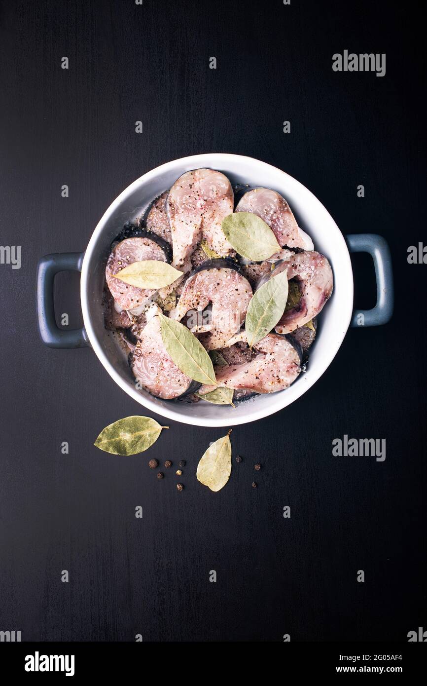 Scheiben leicht gesalzener Makrelenfische mit Piment und Lorbeerblatt auf einem schwarzen Holztisch. Marinierte Makrelen mit Gewürzen salzen. Stockfoto