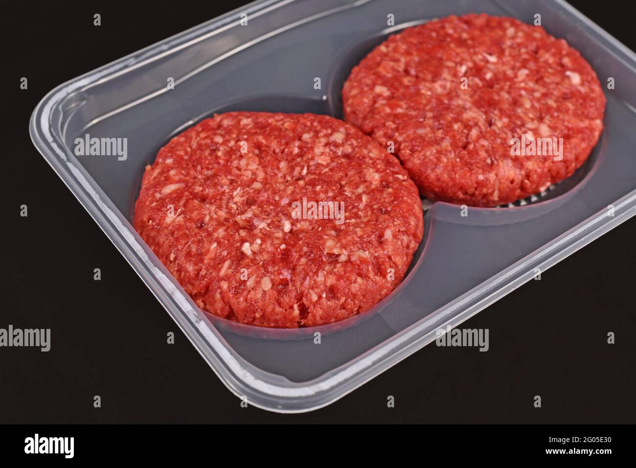 Runde rohe Burger-Patties in der Verpackung auf dunklem Hintergrund Stockfoto