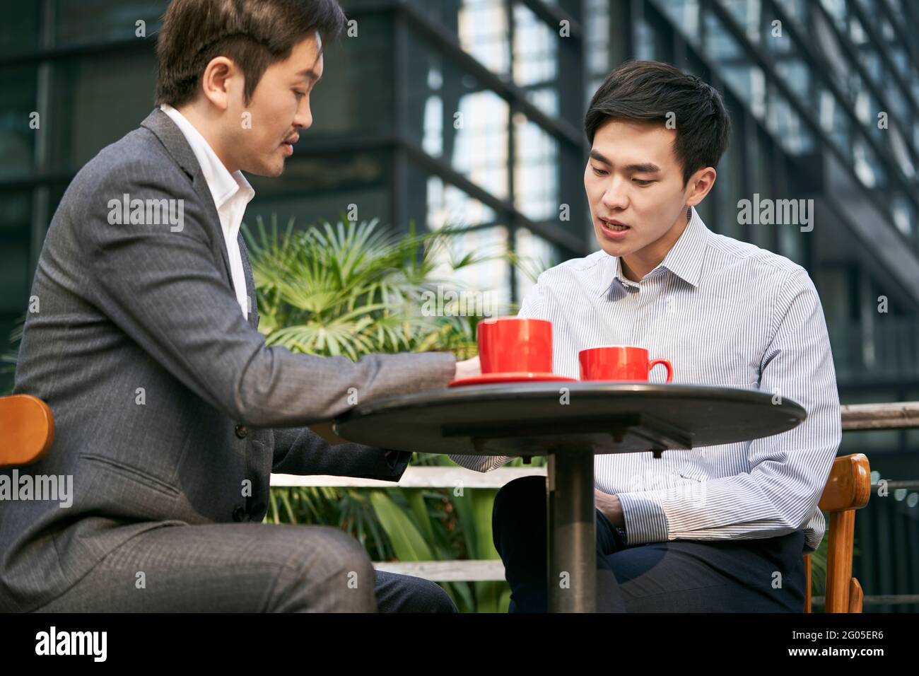 Zwei asiatische Geschäftsleute, die bei einem Kaffee im Freien über Geschäfte diskutieren Kaufen Stockfoto