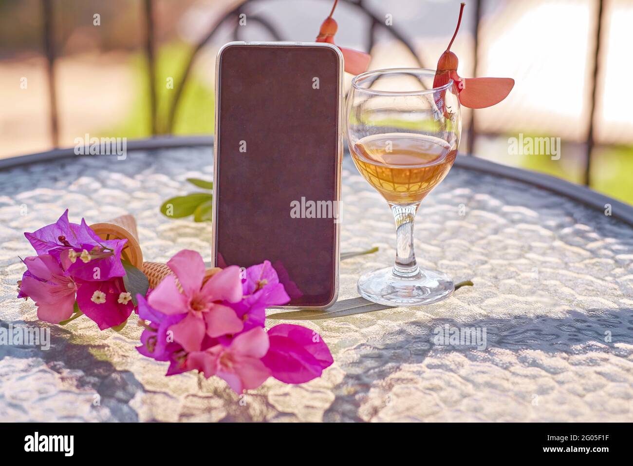Modell eines mobilen Bildschirms mit einem Glas Wein, dekoriert mit frischen, hellen, surrealen Blumen im Sommer. Femininer, flacher Lay. Speicherplatz kopieren. Hochwertige Fotos Stockfoto