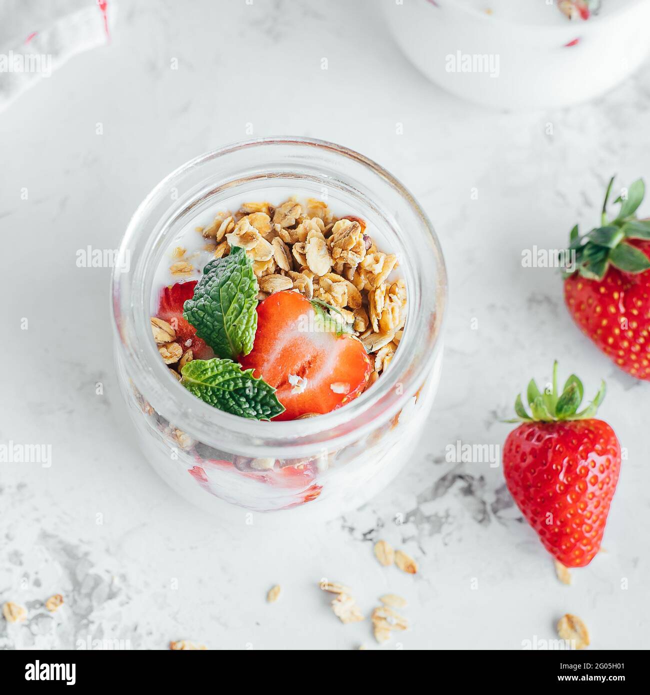 Frühstücksangebot. Glas mit leckeren Parfaits aus Müsli, Erdbeeren und Joghurt auf Marmortisch Stockfoto
