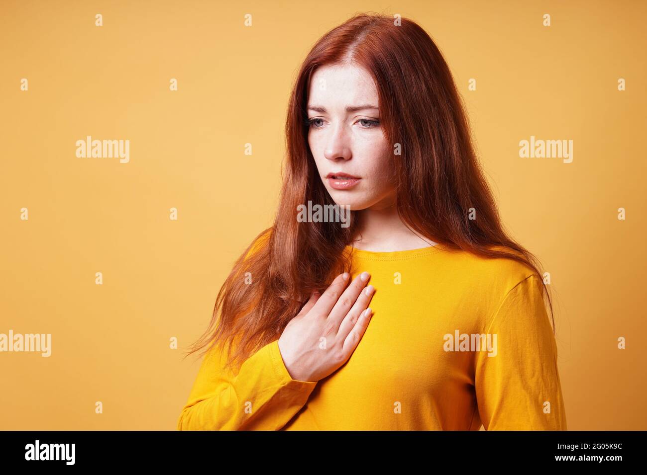 Traurige junge Frau mit der Hand auf der Brust, die Herzschmerz oder Sodbrennen fühlt Stockfoto