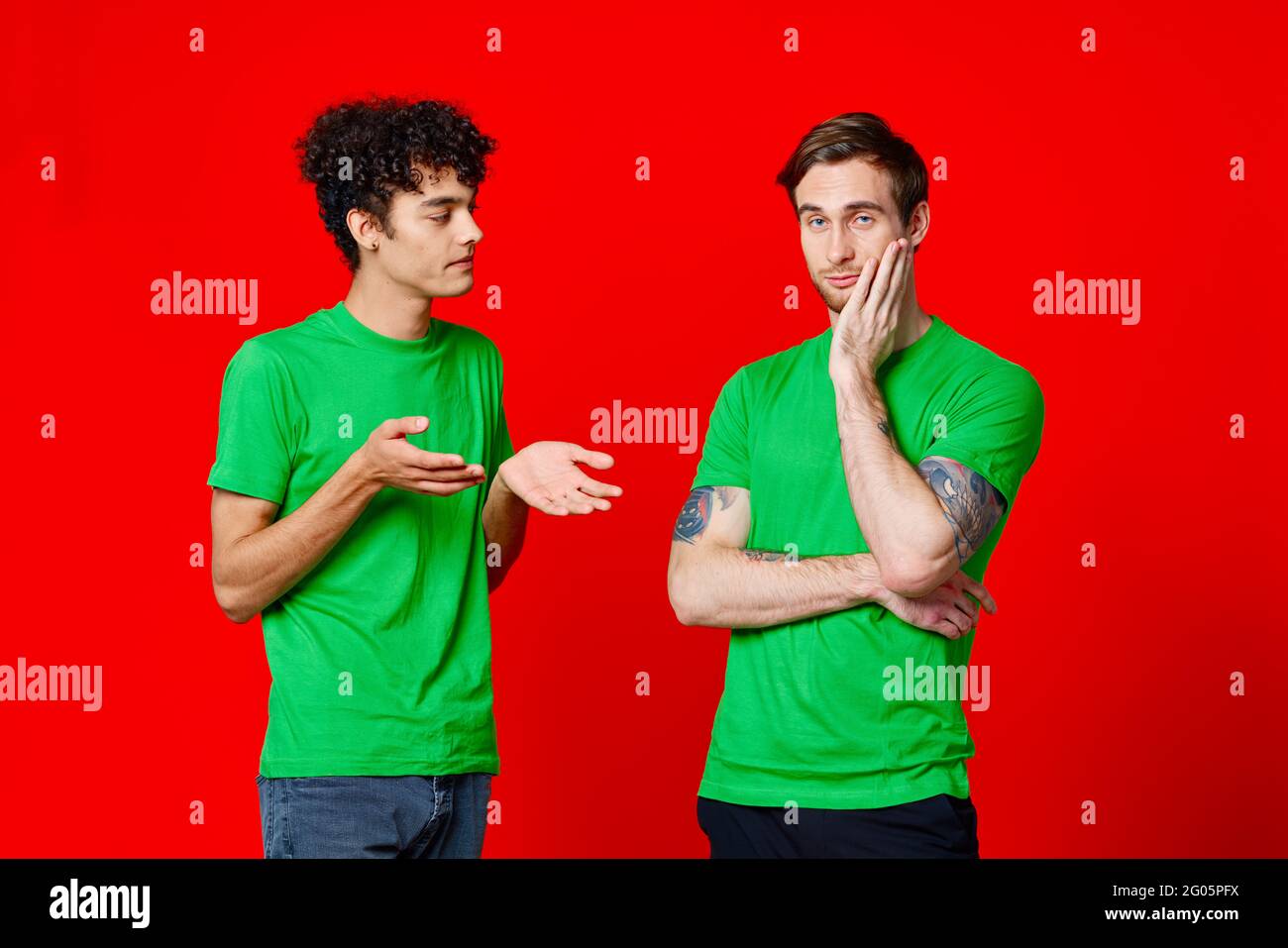 Zwei Männer in grünen T-Shirts stehen neben Communication Friendship Roter Hintergrund Stockfoto