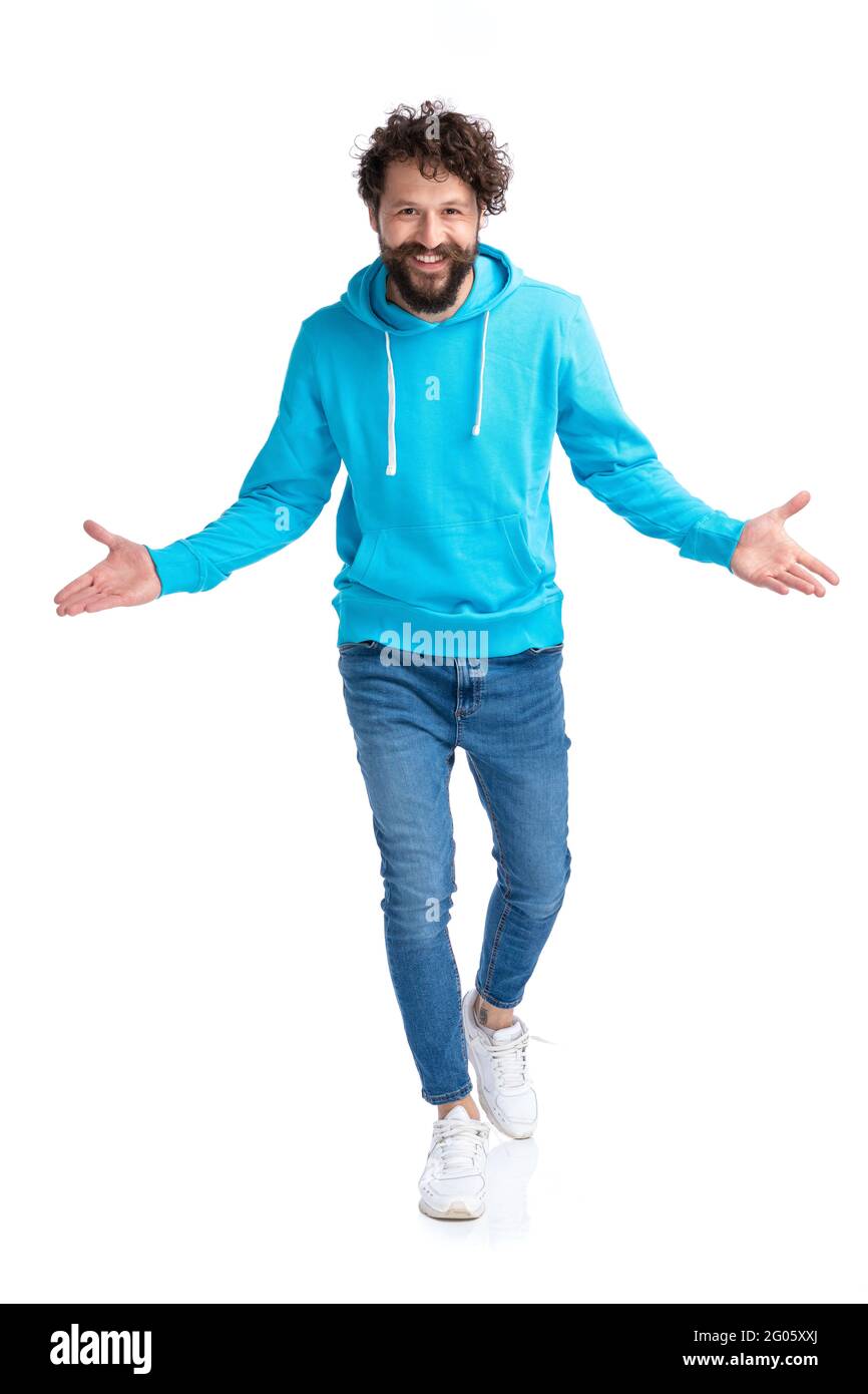 Enthusiastischer bärtiger Mann mit blauem Kapuzenpullover, der die Arme öffnet, umarmt und präsentiert, während er selbstbewusst lächelt und isoliert auf weißem Hintergrund in s läuft Stockfoto